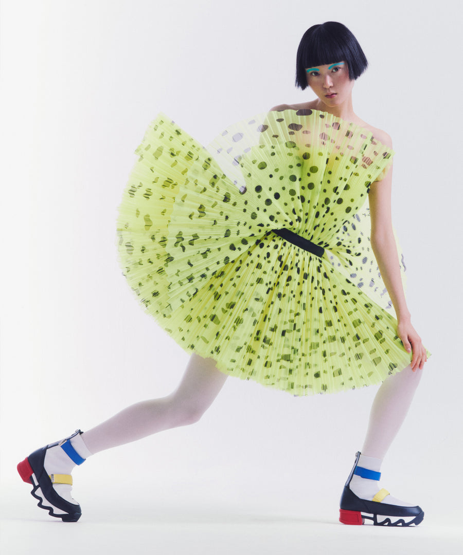 A model wearing iRi VES Multi Primary High Top Sneaker with black polka dot on yellow flared dress and white tights