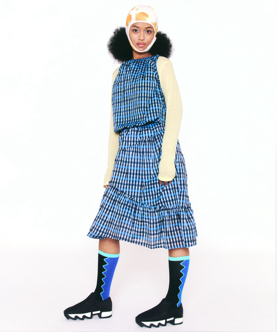 A posing model wearing WES Black Outline Low Top Sneaker with blue ruffled stripe dress and pastel yellow knit top.