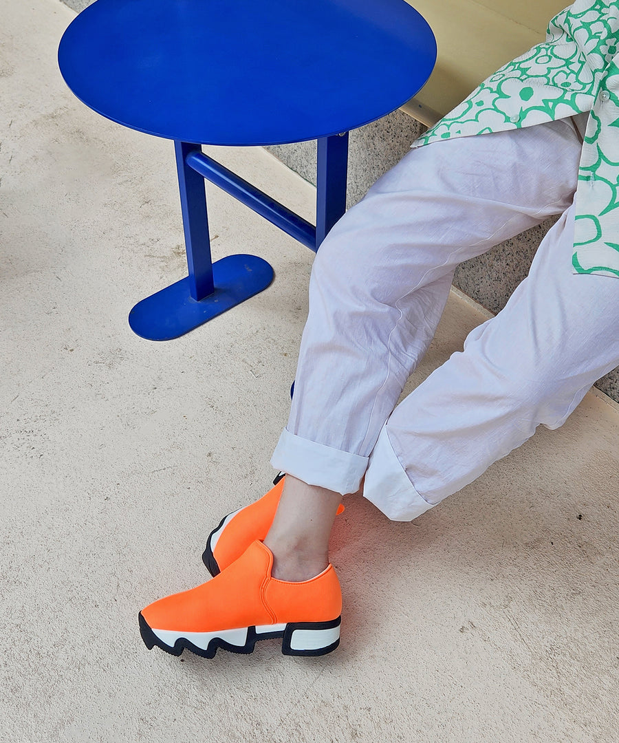 iRi WES I Orange Low Top Sneaker worn by a model sitting on a bench